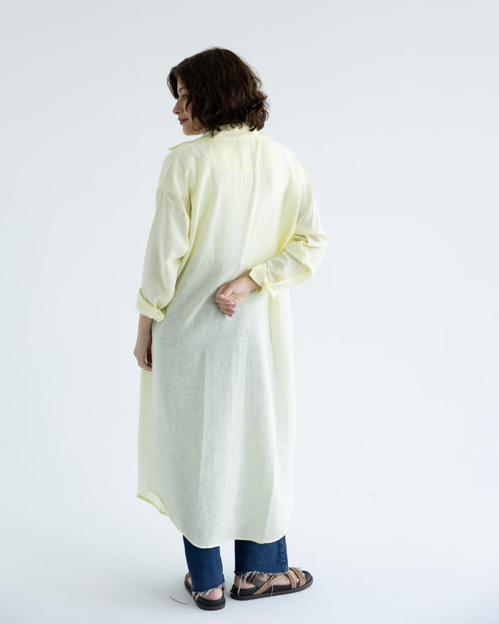 Woman wearing a light-colored long shirt and dark pants on a white background